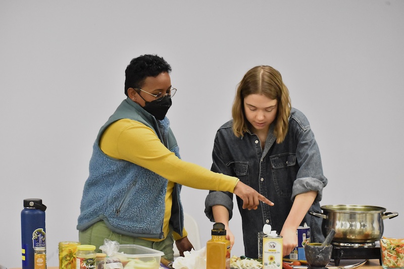 Two people standing behind a table covered with various cooking ingredients.