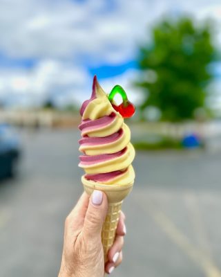 Hand holding an ice cream cone with yellow and red ice cream twisted together with a cherry gummy in the side