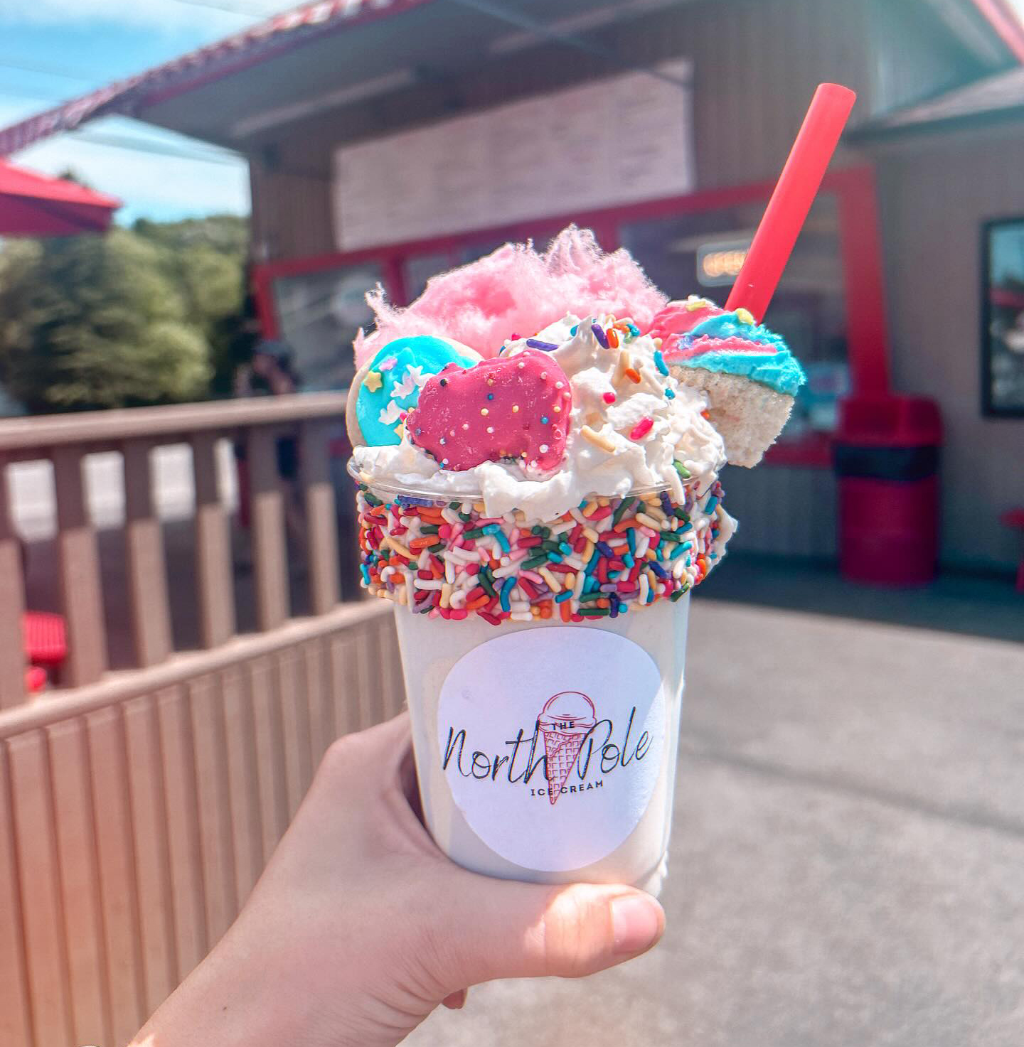 Milkshake with rainbow sprinkles around the edge, pink animal crackers and cotton candy and cake.