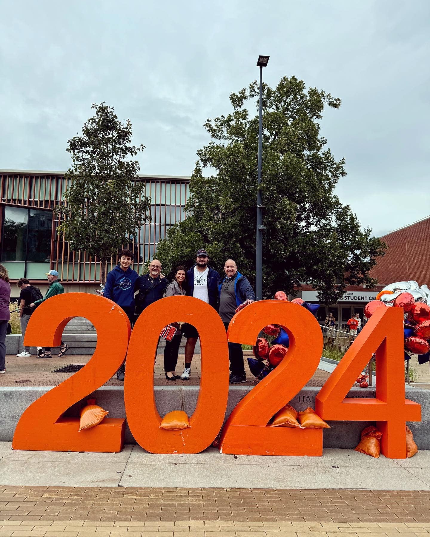 Five people stand behind a large orange 2024 sign in front of the rail.