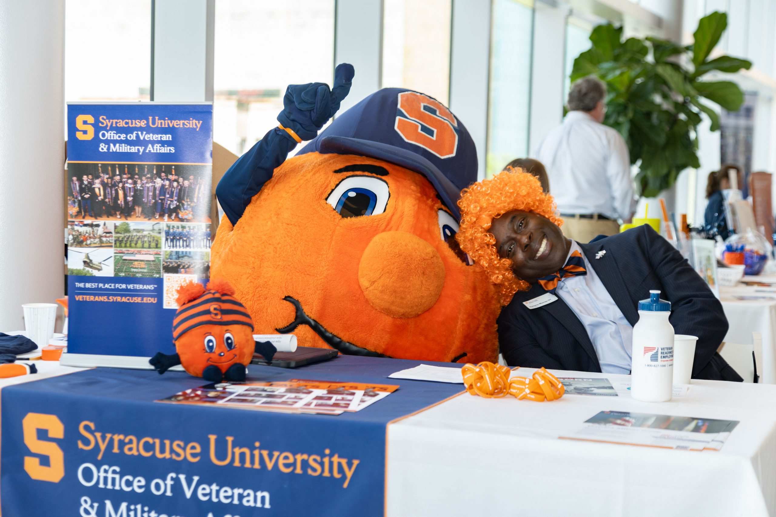 Person with orange wig sitting next to Otto the Orange at a table