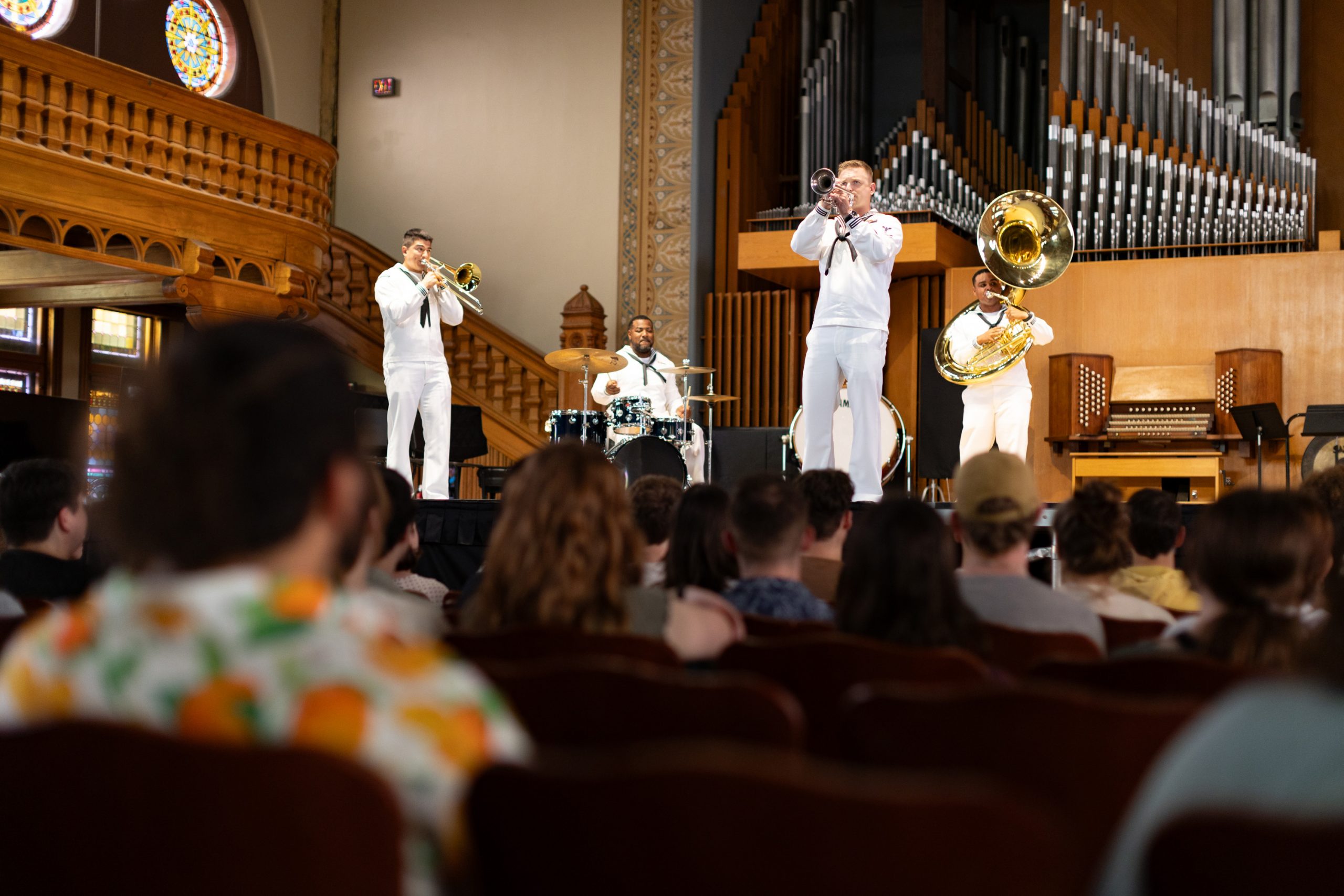 Musicians in white Navy uniforms performing on stage for an audience