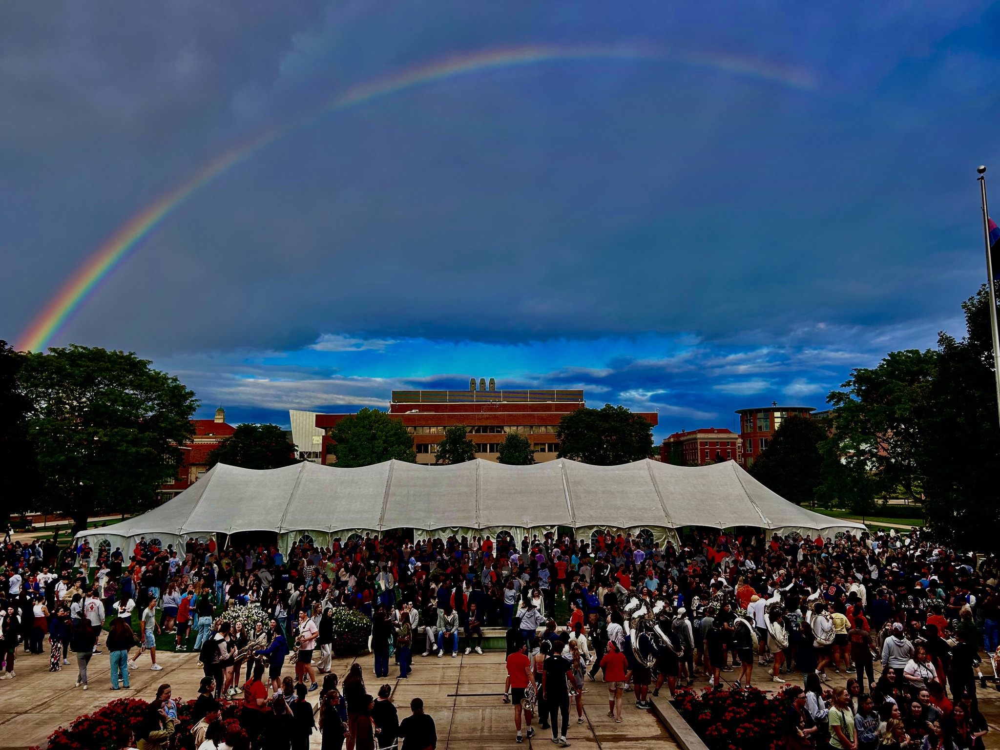 Rainbow over the quad with a big white tent and a large group of people.