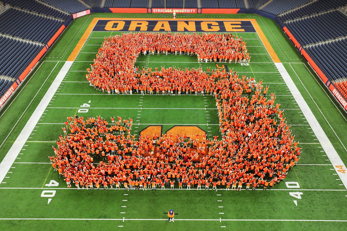 Students in the Class of 2028 pose for their class photo in the shape of an S on the floor of the JMA Wireless Dome.