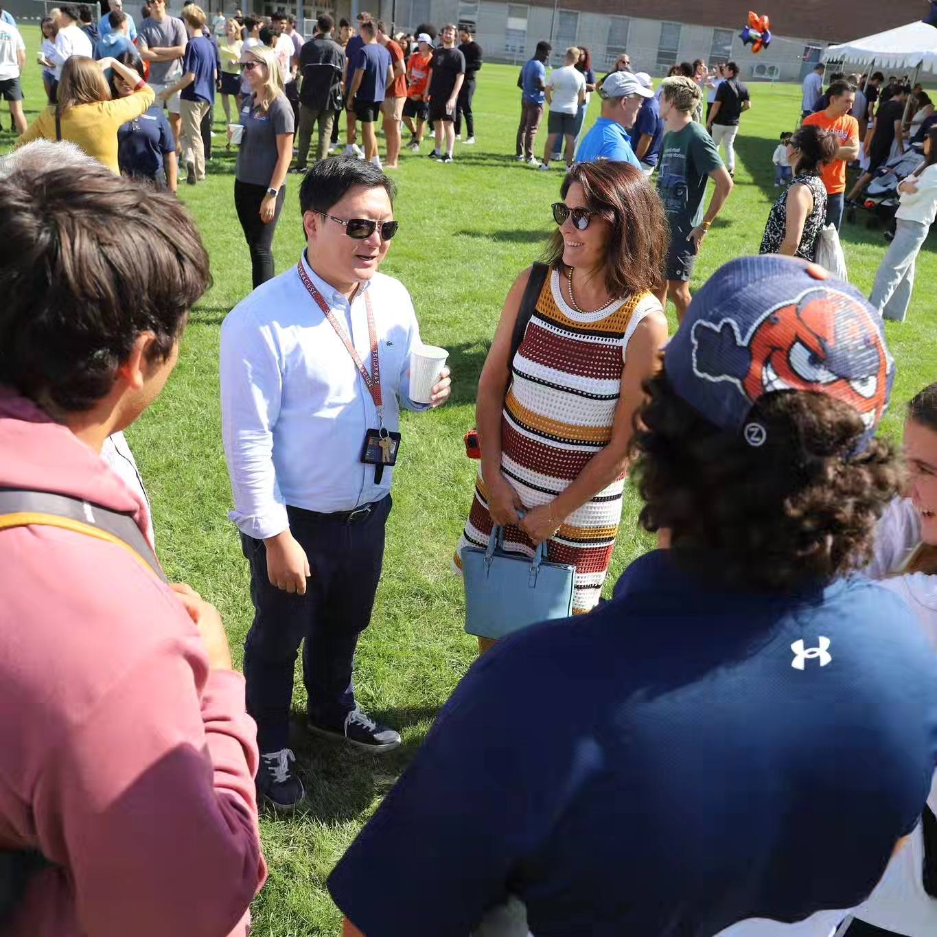 A group of people standing outside on the grass on a sunny day and talking