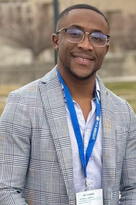 A man smiles for a headshot while standing outside.