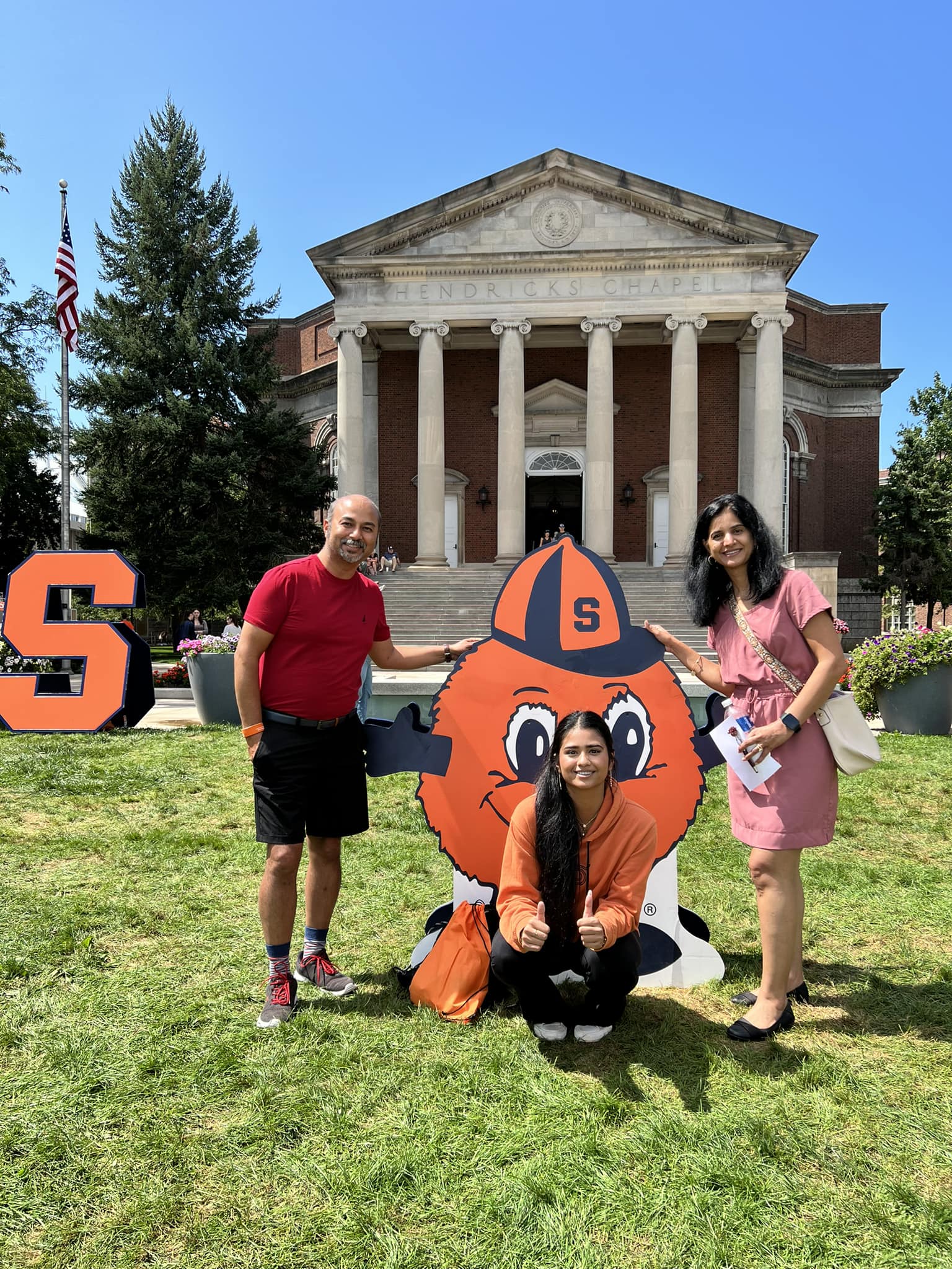 Three people stand on campus with an “Otto the Orange” sign. 