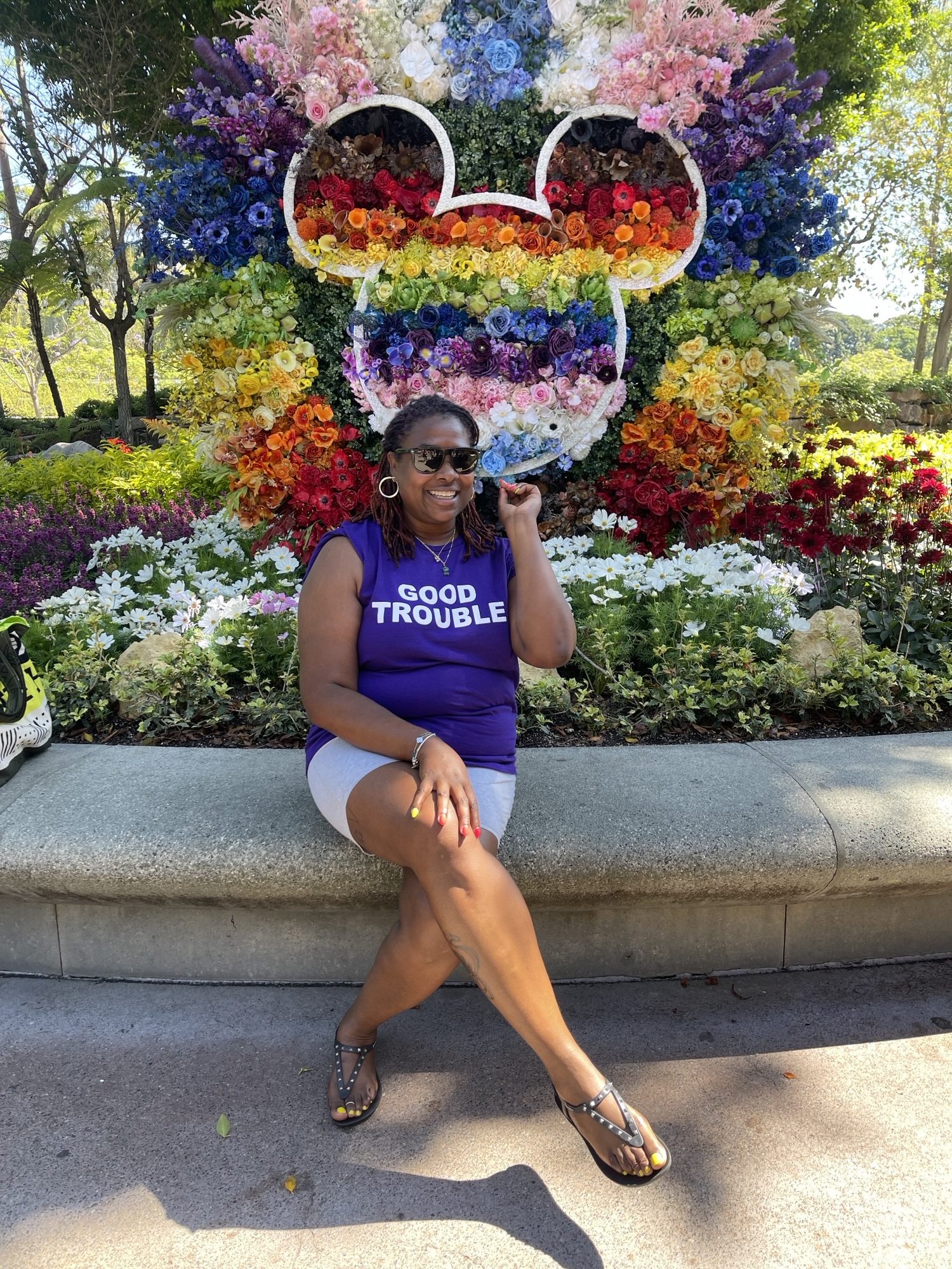 Person sitting in front of a flora display in the shape of mickey mouse.