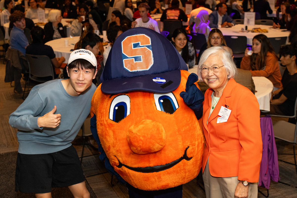 Two people stand with Otto the Orange