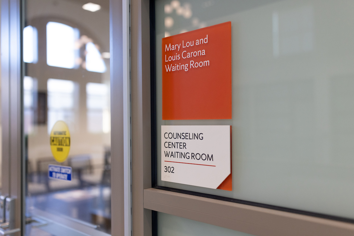Sign outside of a room that says Mary Lou and and Lois Carona Waiting Room written in white on an orange background and below that on a white sign says Counseling Center Waiting Room 302.
