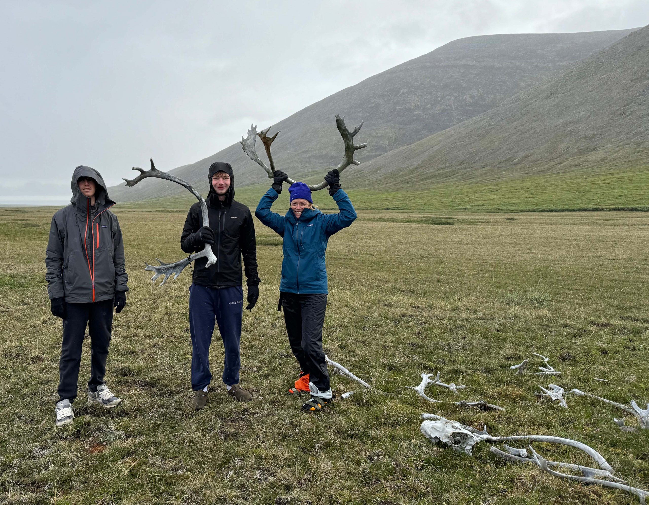 Three people standing in the wilderness holding up antlers. 