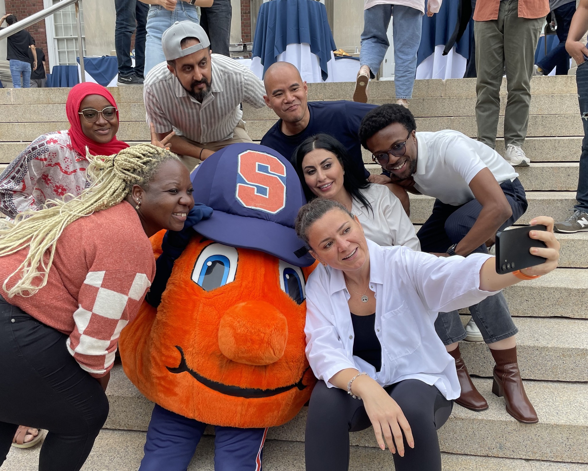 Group of people gathered for a photo sitting on the stairs with Otto the Orange. 