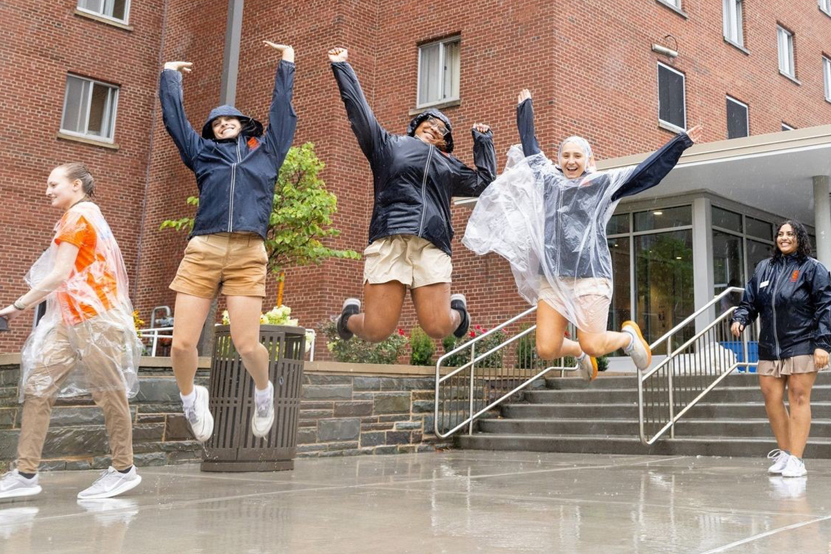 Three students jump for joy in the rain after helping students during Syracuse University's move-in.