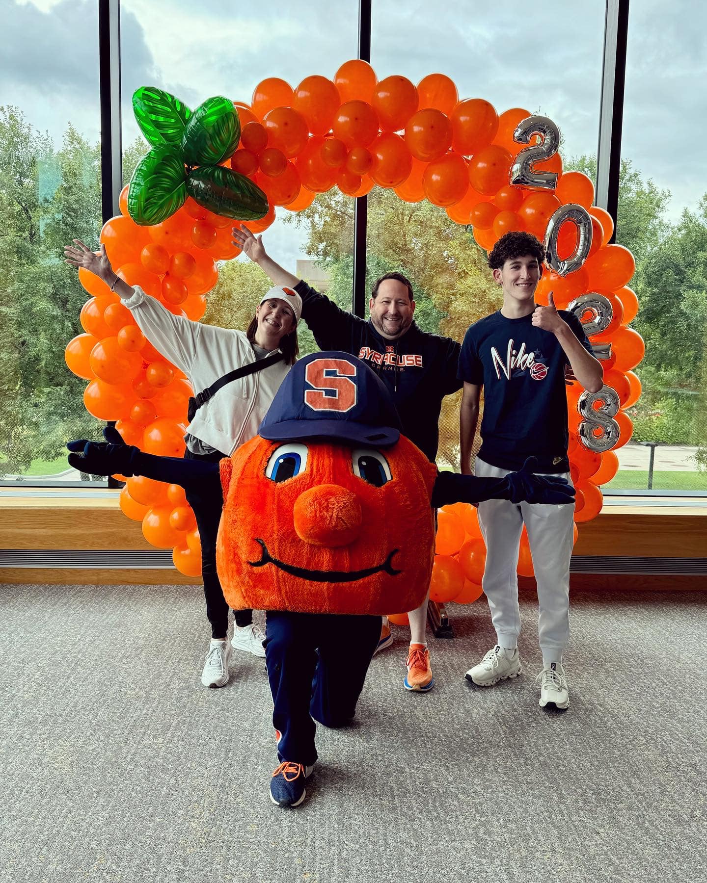 Inside, three people with an orange balloon arch and Otto the Orange posing for the photo. 