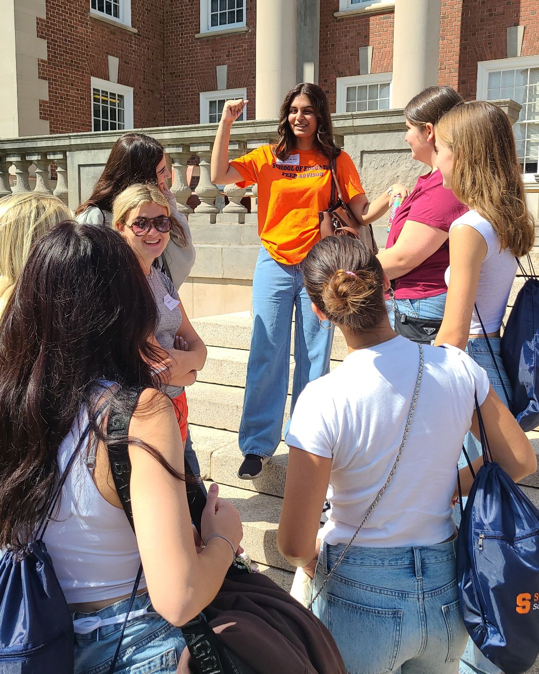 Student in orange t-shirt talks to a group of students. 