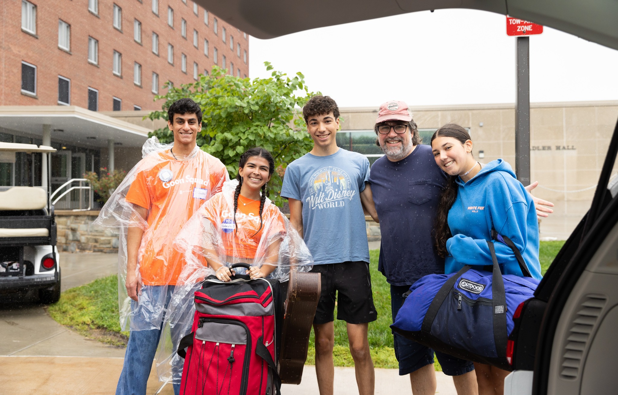 Five people are standing next to a car with a suitcase.