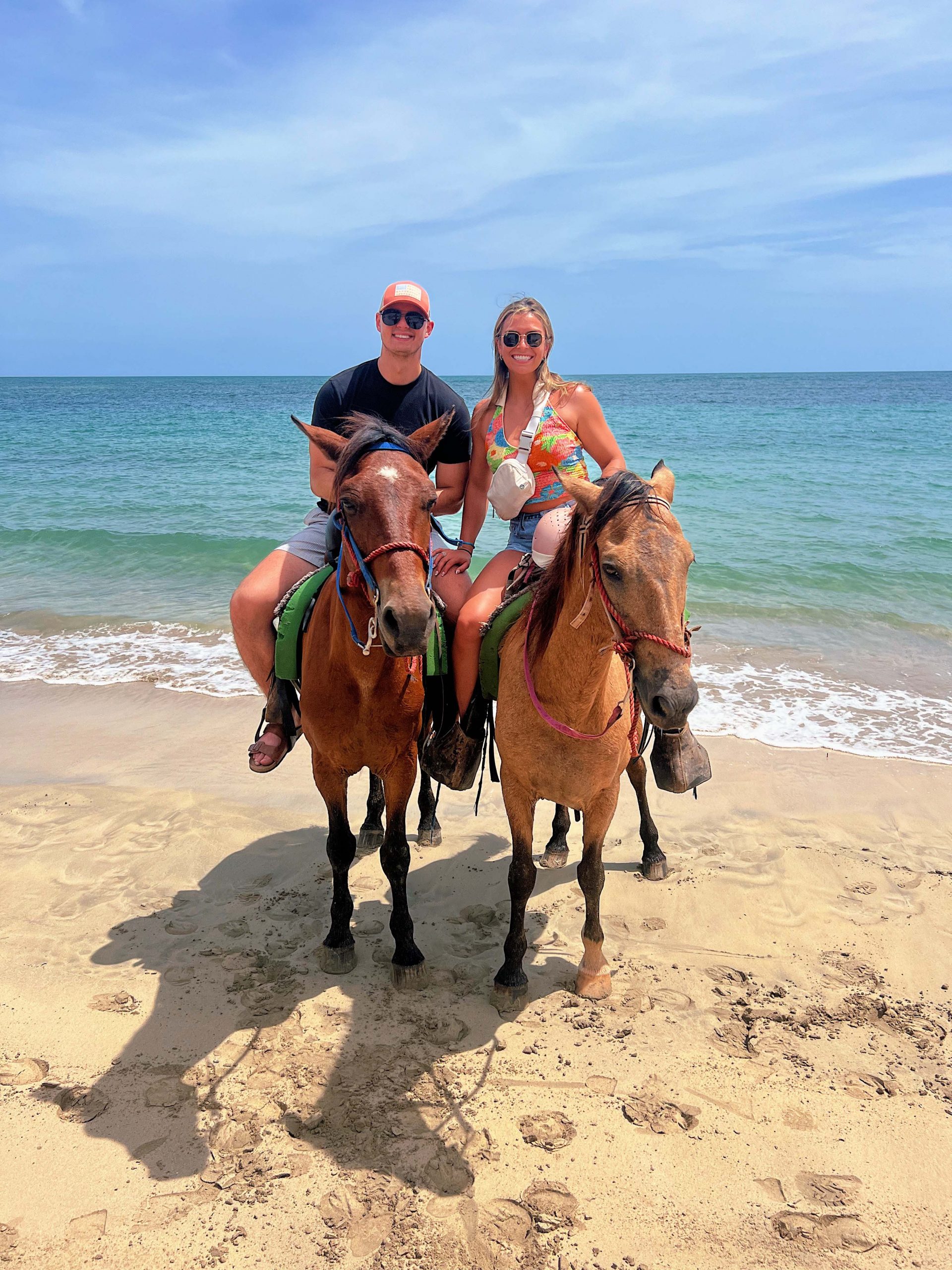 Two people sitting on horses at the beach with the ocean in the background.