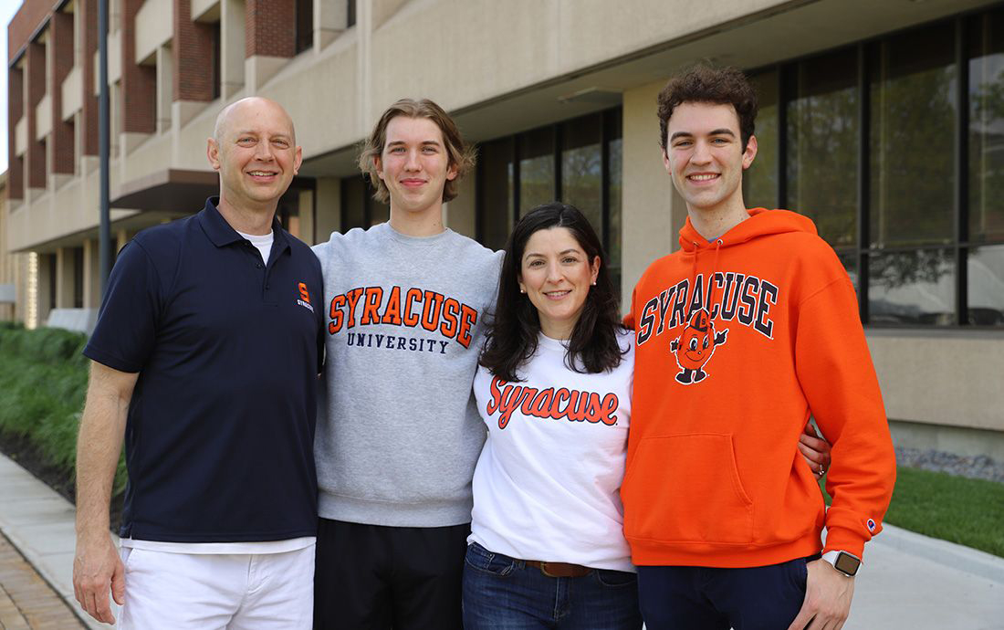 Vanderwege family (mother, father and two sons) pose together outside of Link Hall in Syracuse attire