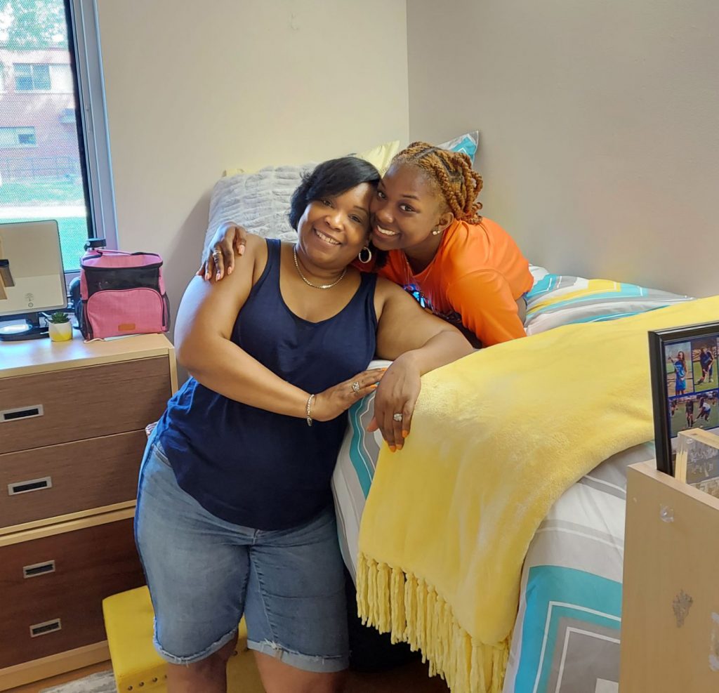 Student laying on their bed in a dorm room hugging their mom.