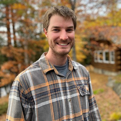 A man smiles while posing for a photo outside.