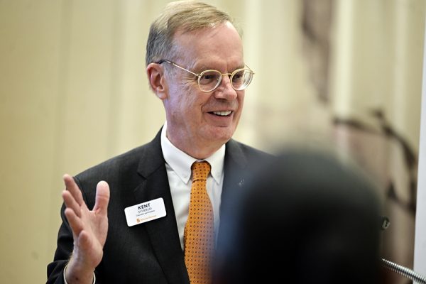 Chancellor Kent Syverud in a suit with an orange tie and name tag gestures with his hand while smiling at an event in Washington, D.C. A blurred audience member appears in the foreground.