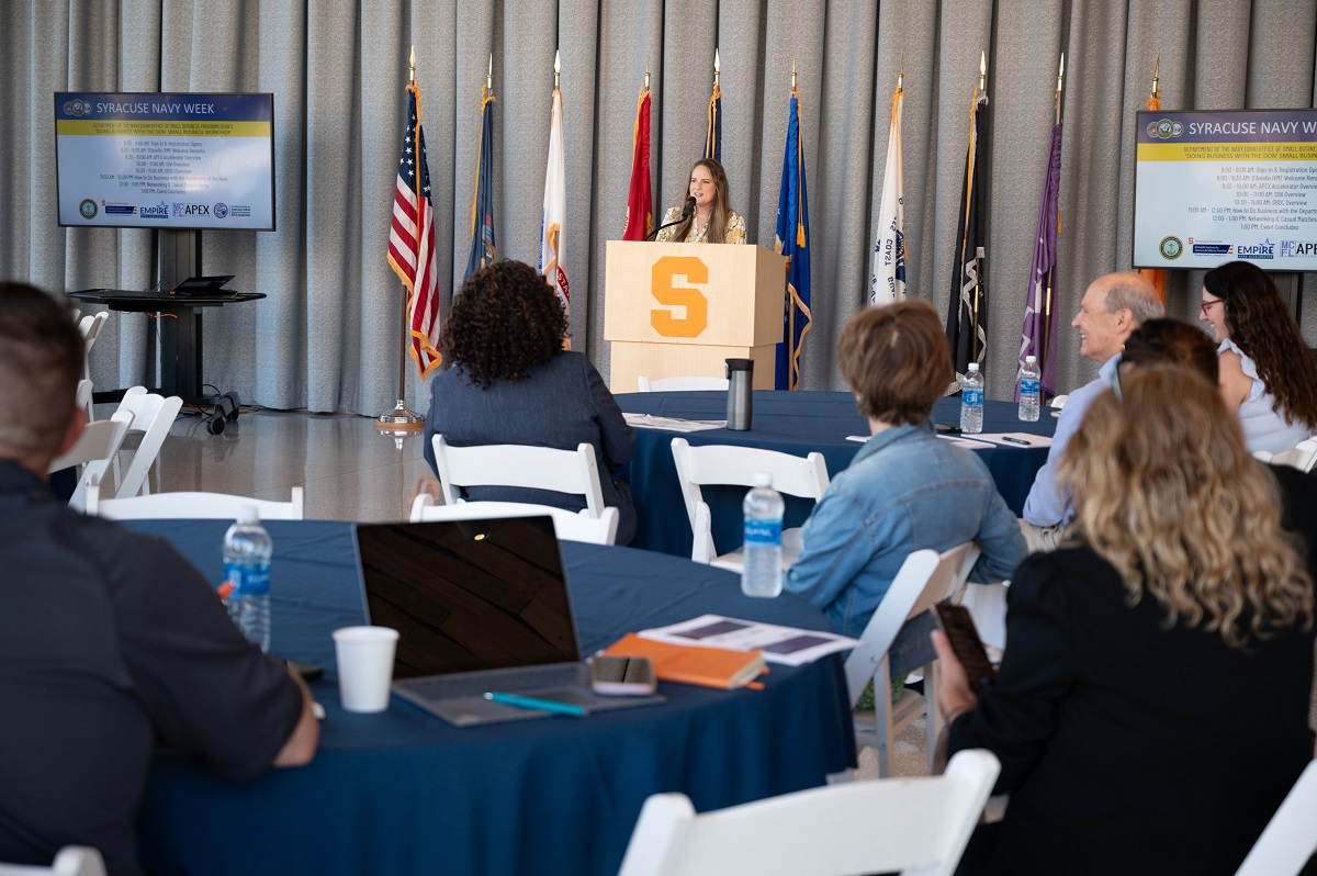 person at podium speaking in front of people seated at tables