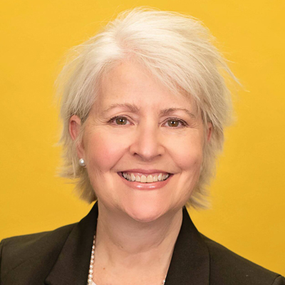 A woman smiles for a headshot in front of a yellow wall.