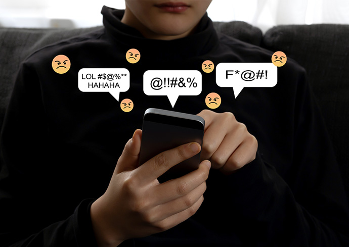 A person using a smartphone with angry face emoticons and messages containing expletives visible on the screen