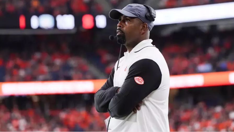 A man stands with his arms crossed while coaching a football game.