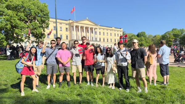 group of students pose holding Norwegian flags outside a large building