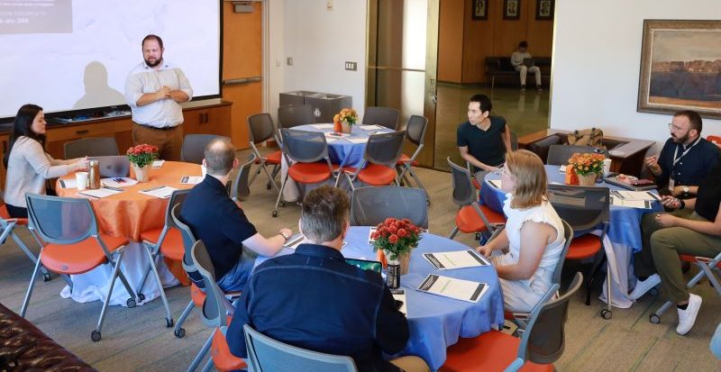 person speaking to an assembled group of people seated at tables