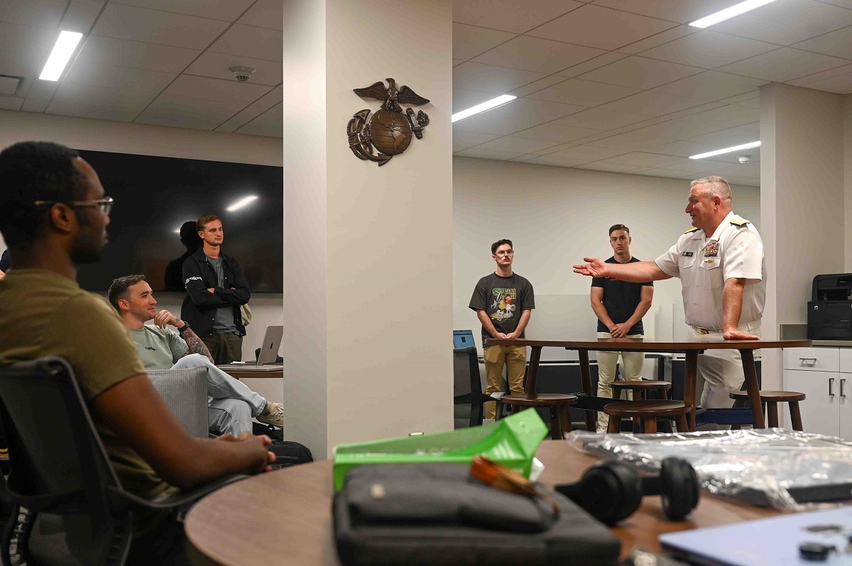 person in uniform speaking to a group of people in a classroom