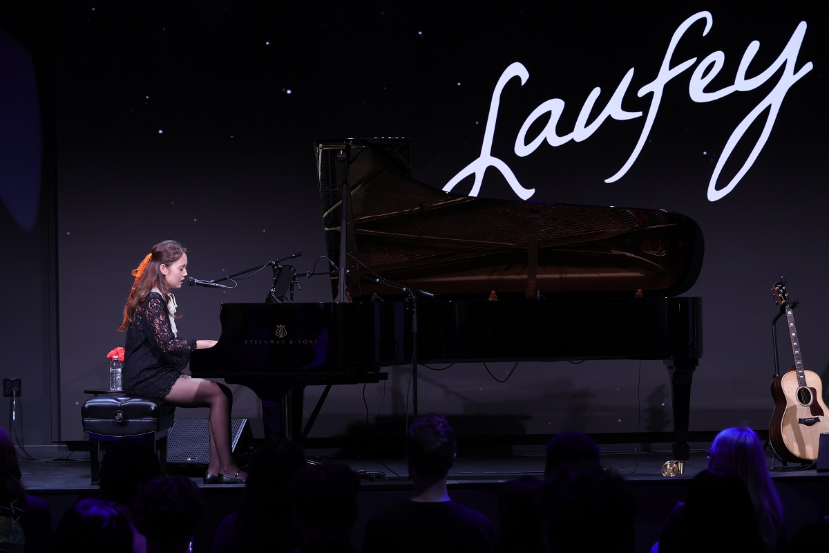 person sitting at a piano in front of large sign with word Laufey