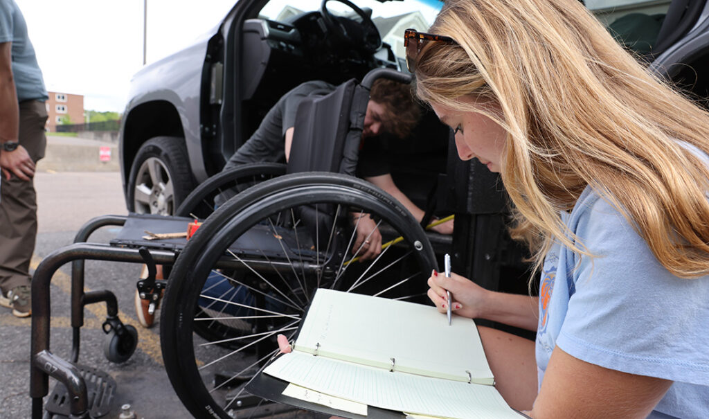 Person next to an empty wheelchair writing in a notebook. 