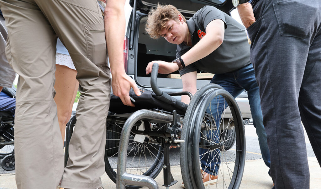 People adjusting an empty wheelchair.