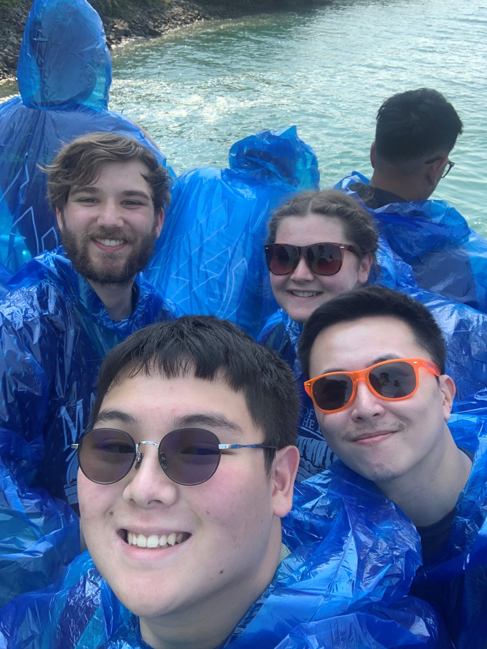 Group of people in blue ponchos, enjoying a boat ride near Niagara Falls, taking a selfie with water in the background.