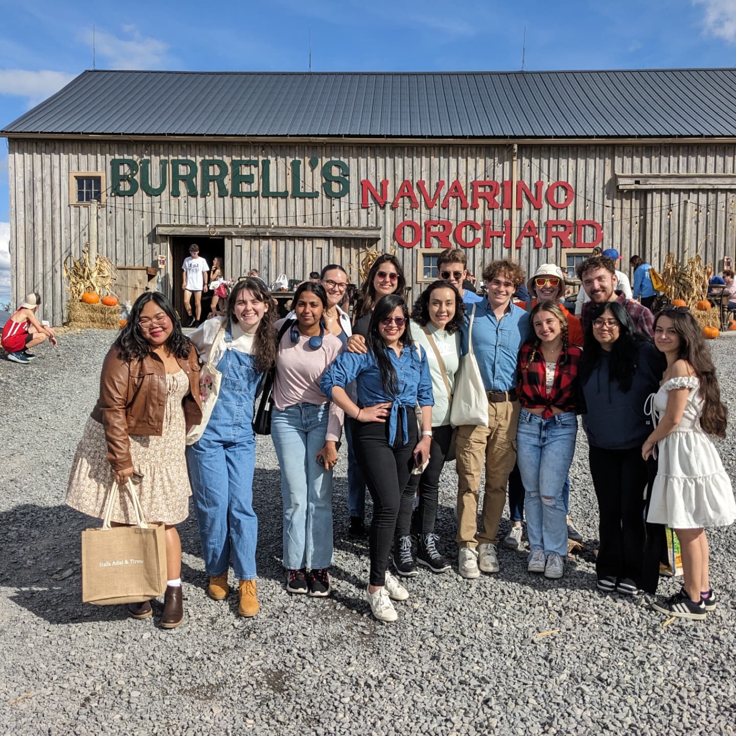 Group of people smiling in front of Burrell's Navarino Orchard on a sunny day.