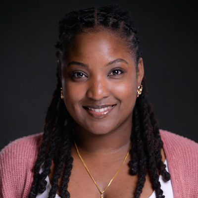 A woman in a pink sweater smiles for a studio headshot against a dark neutral backdrop