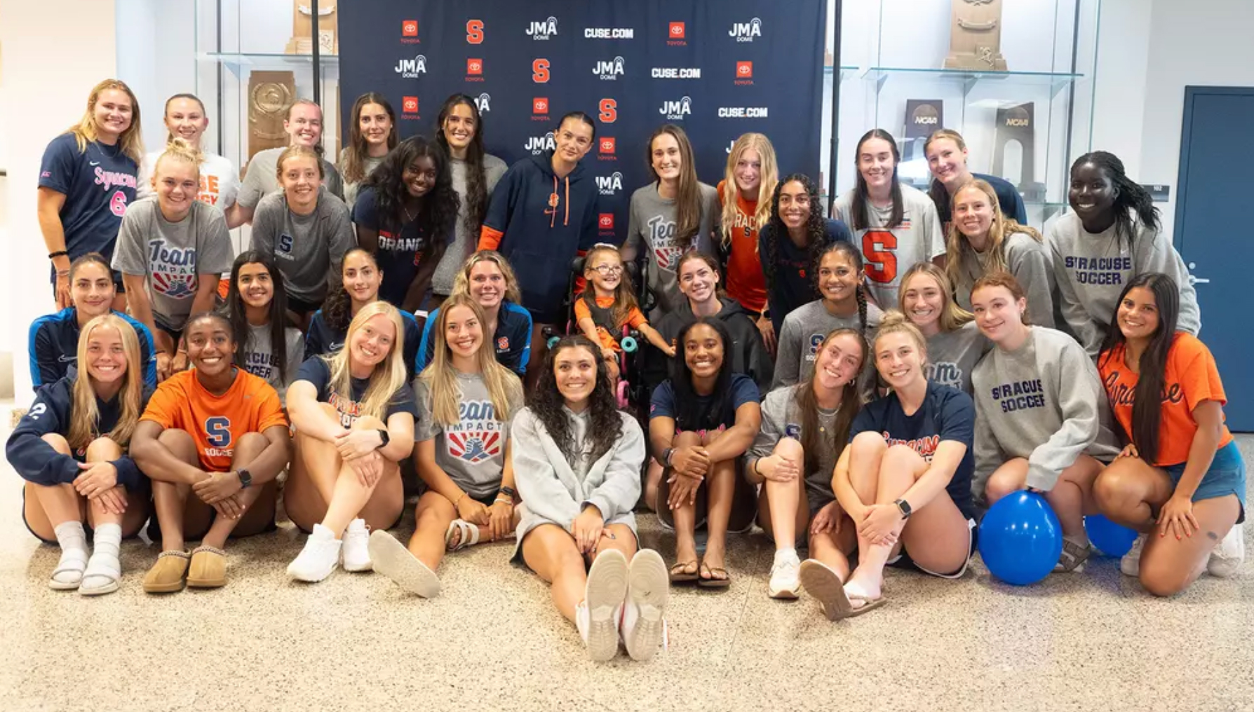 Group of Syracuse University athletes posing indoors with a "Team Orange Soccer" banner in the backdrop.