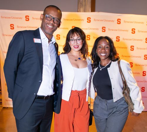 man at left meets with two women at a reception, all facing camera