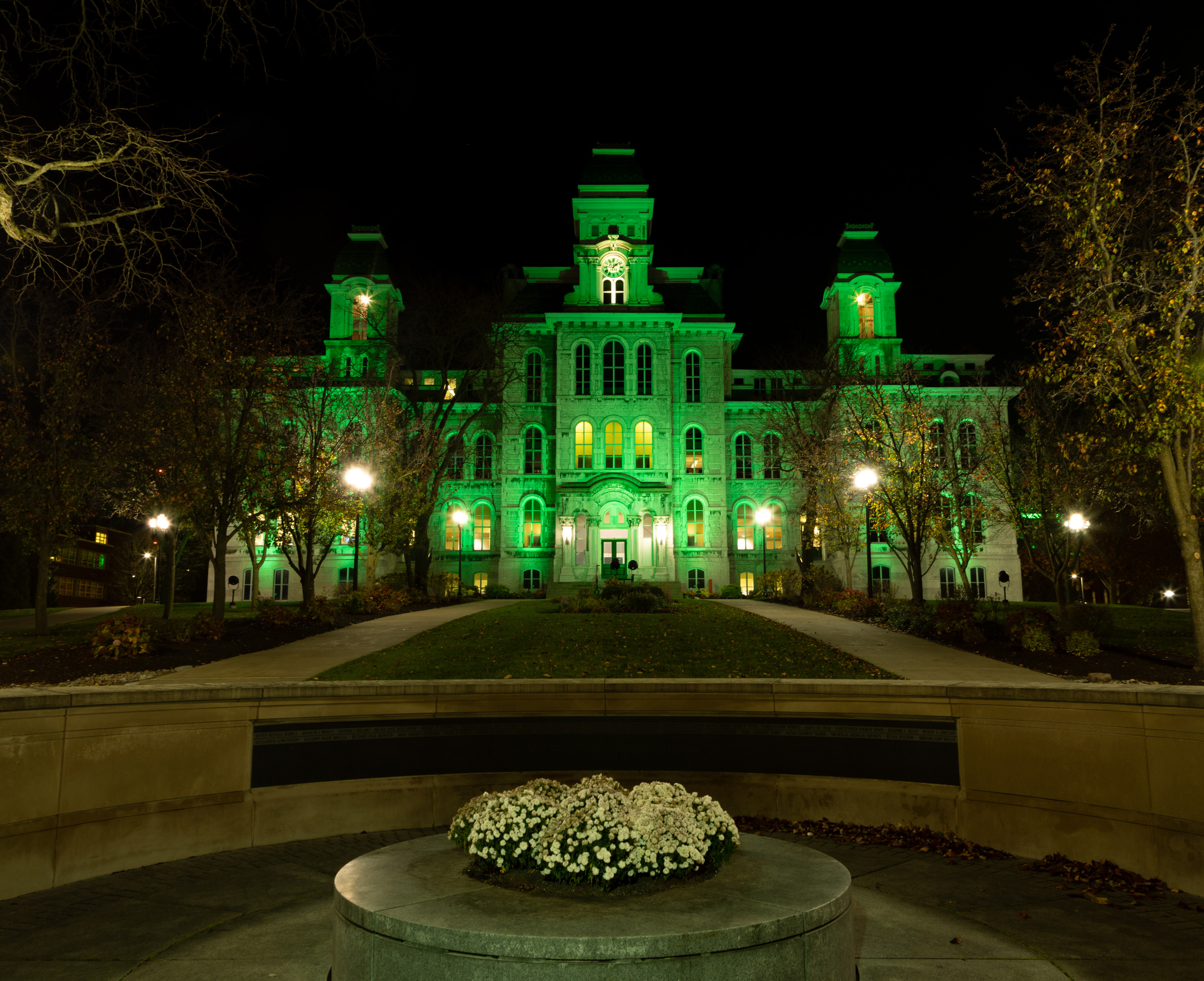 Syracuse University’s Hall of Languages lit up with green lights in honor of the national “Operation Green Light” campaign in honor of Veterans Day. Taken from the Wall of Remembrance, the Hall of Languages is set in the background and flanked by trees on either side of the image.