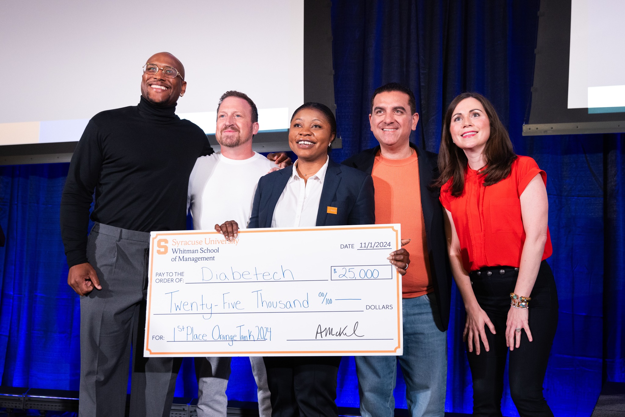 Five people smiling at a presentation event, holding a large ceremonial check to Diabotech from Syracuse University Whitman School of Management for $25,000, dated October 20, 2024.