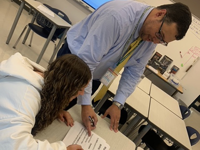 A teacher assisting a student with schoolwork in a classroom.