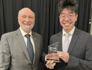 Two people standing side by side with one person holding an award.