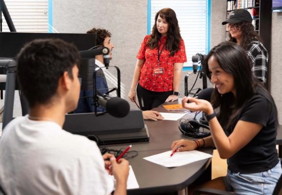 woman among several students at radio broadcast booth