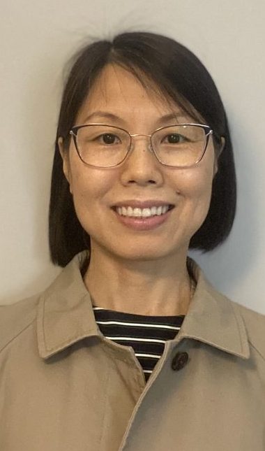 A woman smiles for a headshot while standing in front of a white wall.