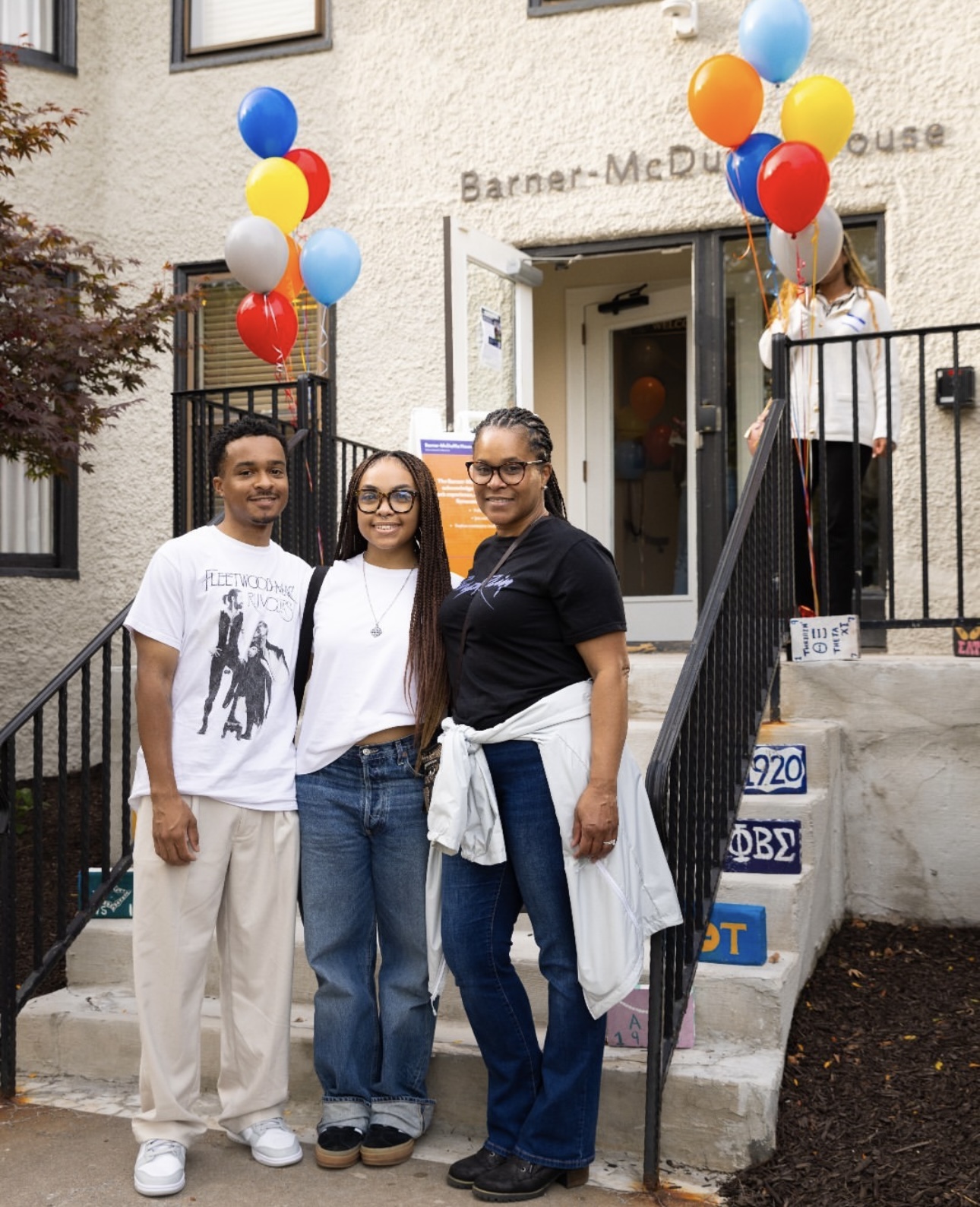 Three individuals posing for a photo on steps outside the Barner-McDuffie House, decorated with colorful balloons.