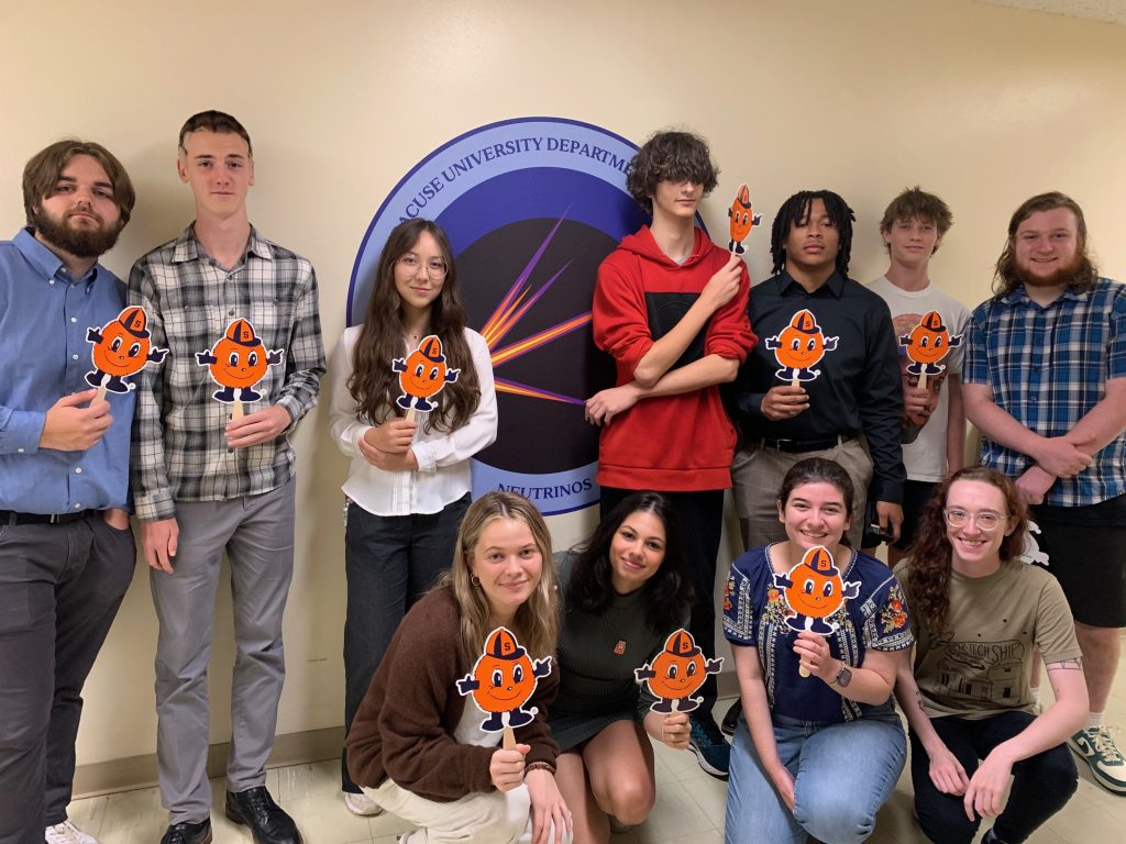 Group of students holding Otto the Orange signs in front of a blue banner.