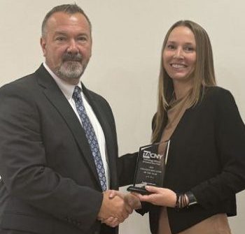 Two people standing together shaking hands with one person holding an award