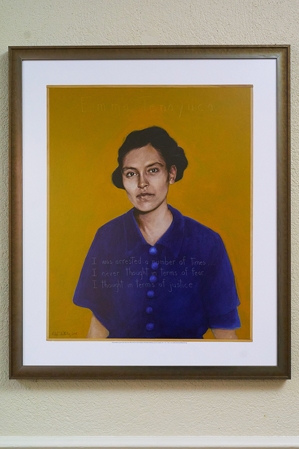 A framed portrait of a woman, Emma Tenayuca, with dark hair, wearing a blue shirt, on a yellow background. Text on the image reads: "I was arrested a number of times. I never thought in terms of fear. I thought in terms of justice."